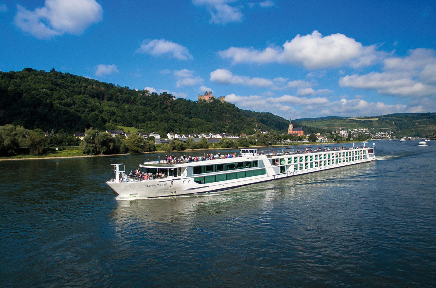 Luxury river cruise ship sailing past green landscape, under a blue, lightly cloudy sky
