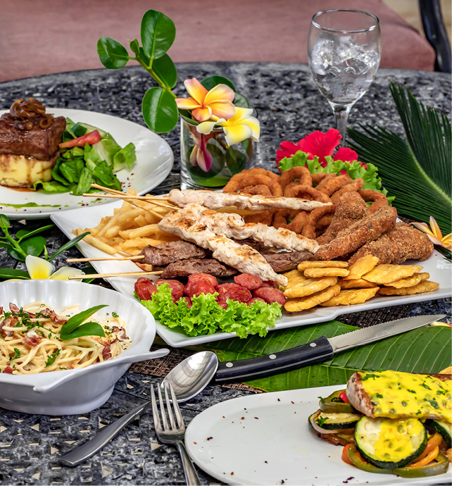 Plates of traditional Caribbean dishes on a table with palm leaves and hibiscus flowers 