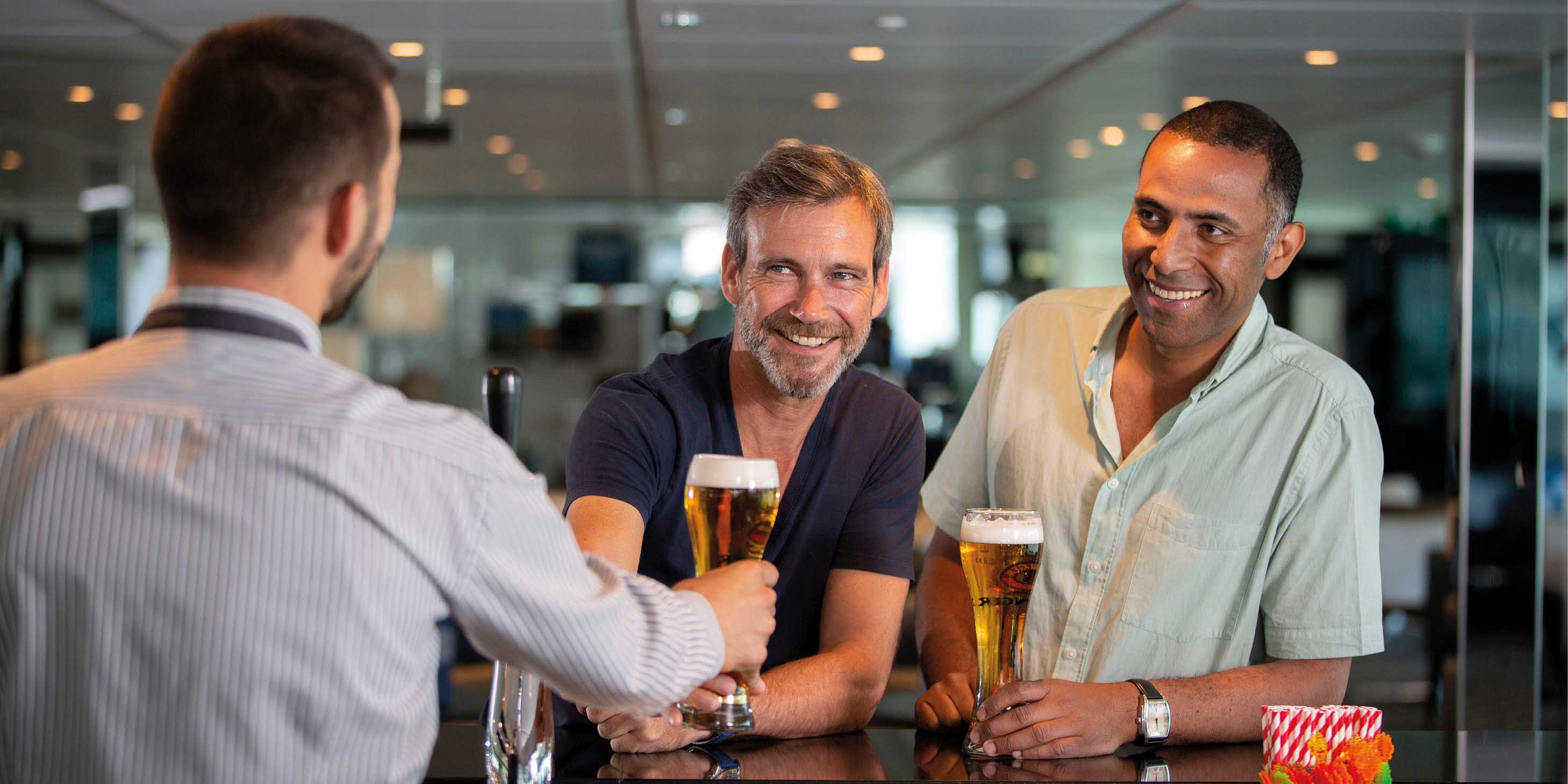 Two men smiling at a bartender, as he serves them beer at the bar 