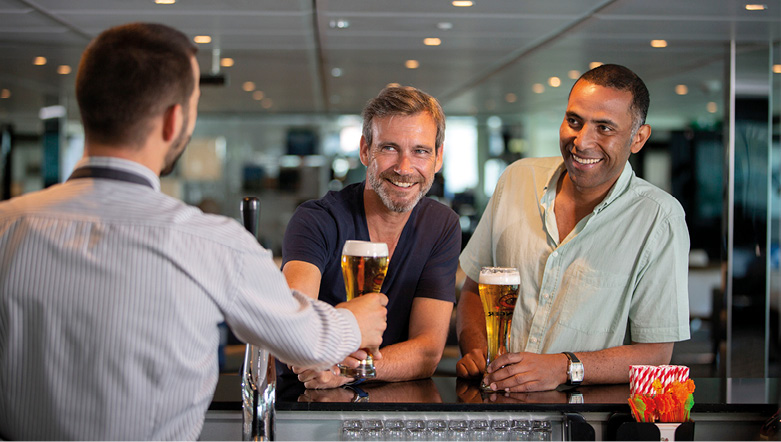 Two men smiling at a bartender, as he serves them beer at the bar 