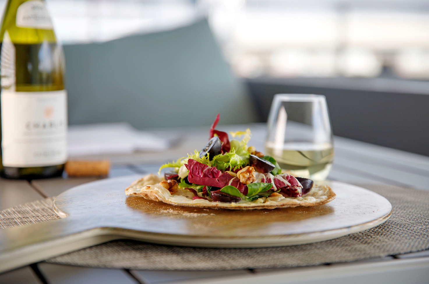 Flatbread topped with fresh salad and a bottle of white wine
