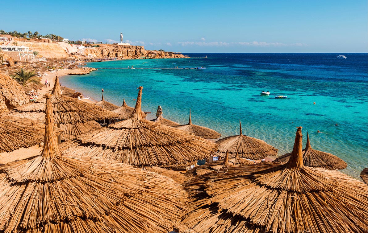 straw thatched parasols lining the curved beachfront on Sharm-el-Sheikh with vibrant blue waters in the background