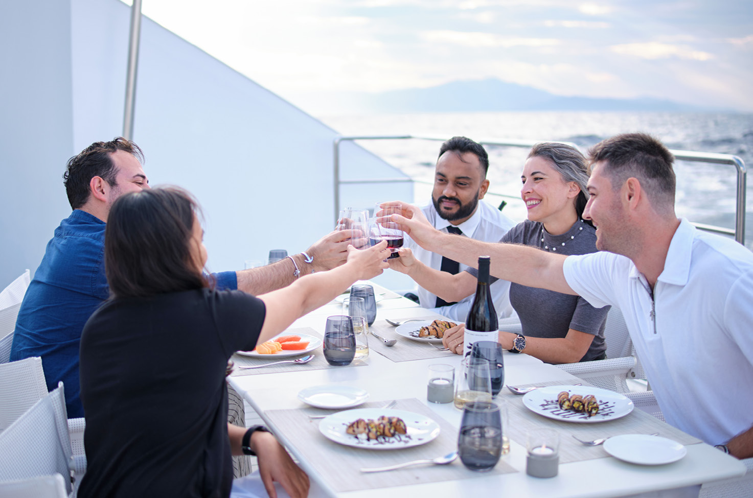 Five guests enjoying their dinner outdoors and cheering with their glasses 