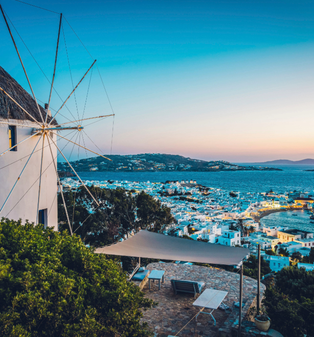 A view of a windmill in Mykonos overlooking the coastline of the city as the sun sets. 