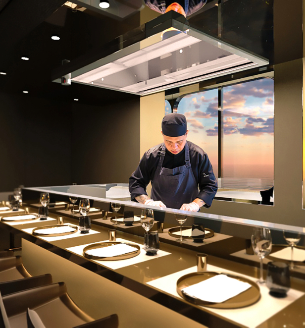 A chef shown preparing dishes on board an Emerald Star-Ship whilst the sun sets on the ocean waters behind him. 