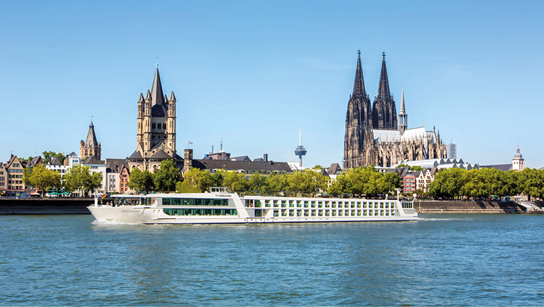 Emerald Cruises ship can be seen sailing along the river bank. The sky is clear and blue.