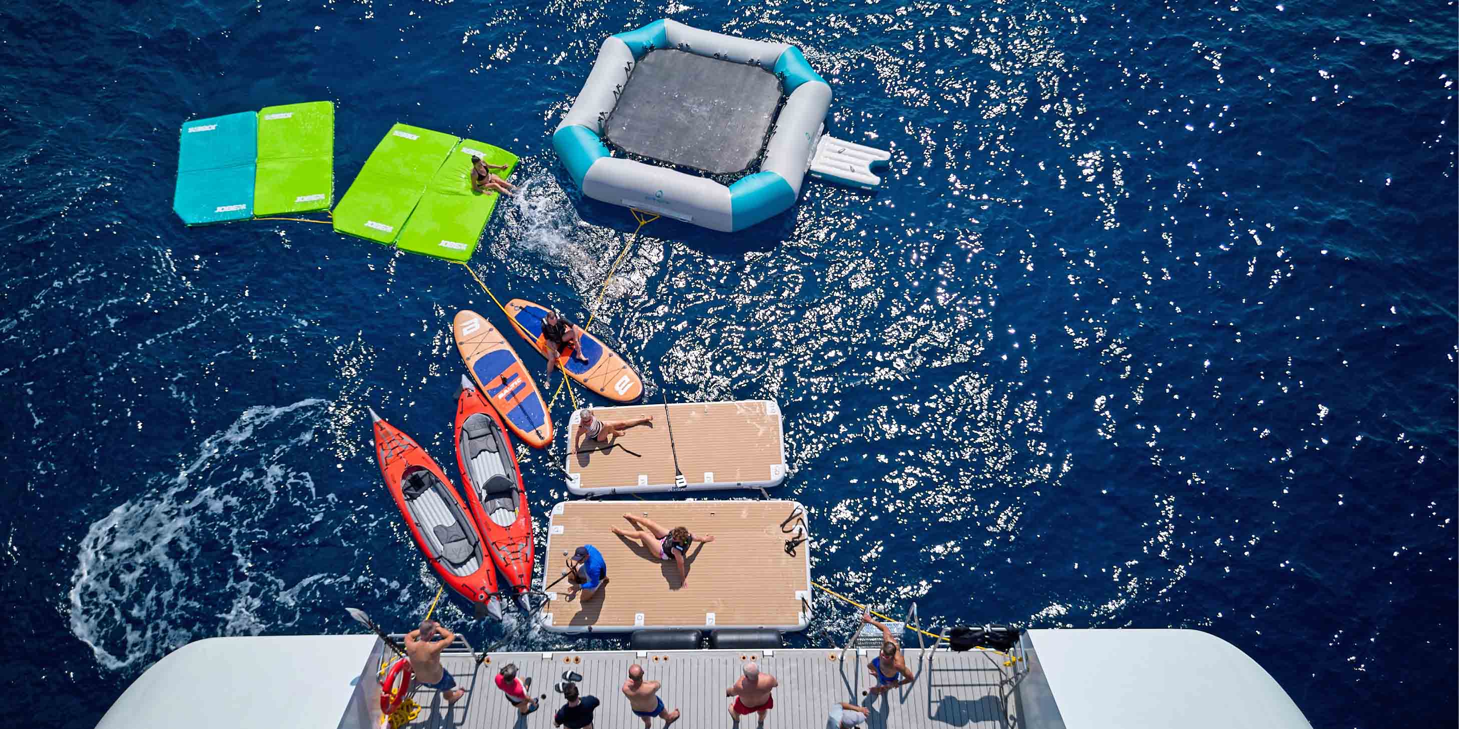 aerial view of a marina platform at the rear of a superyacht with a trampoline, stand up paddle boards and sea kayaks in the water