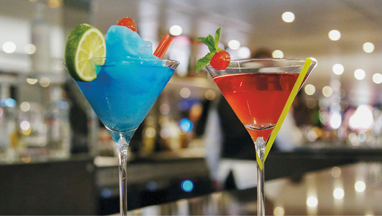 Red and blue cocktails with fruit garnishes on a bar