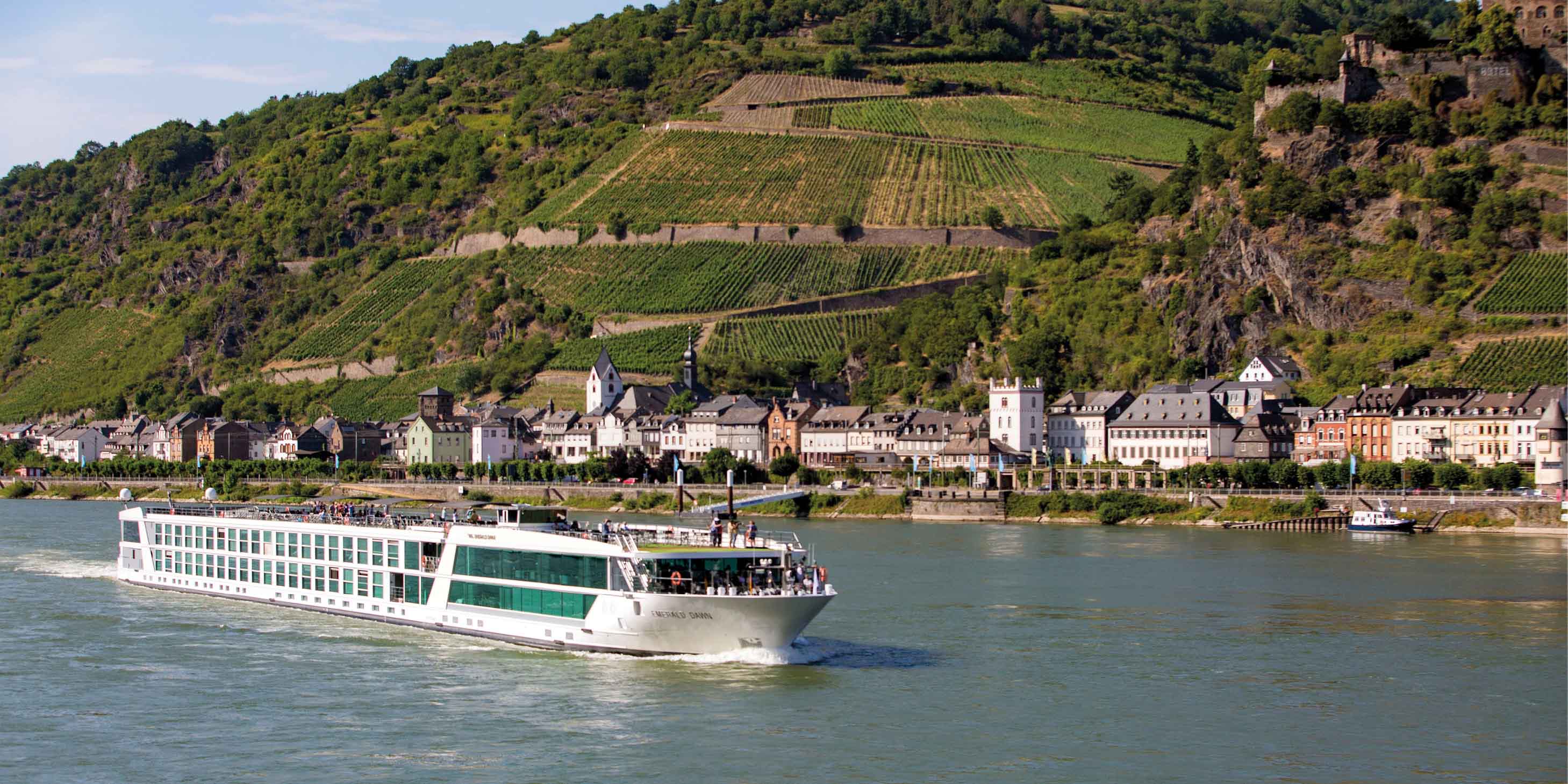 Luxury cruise ship sailing the Rhine River past a quintessential Europe town, with rolling hills in the background