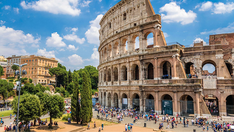 A side view of the Colosseum in Rome, with people lined up outside under cloudy blue skies on a sunny day
