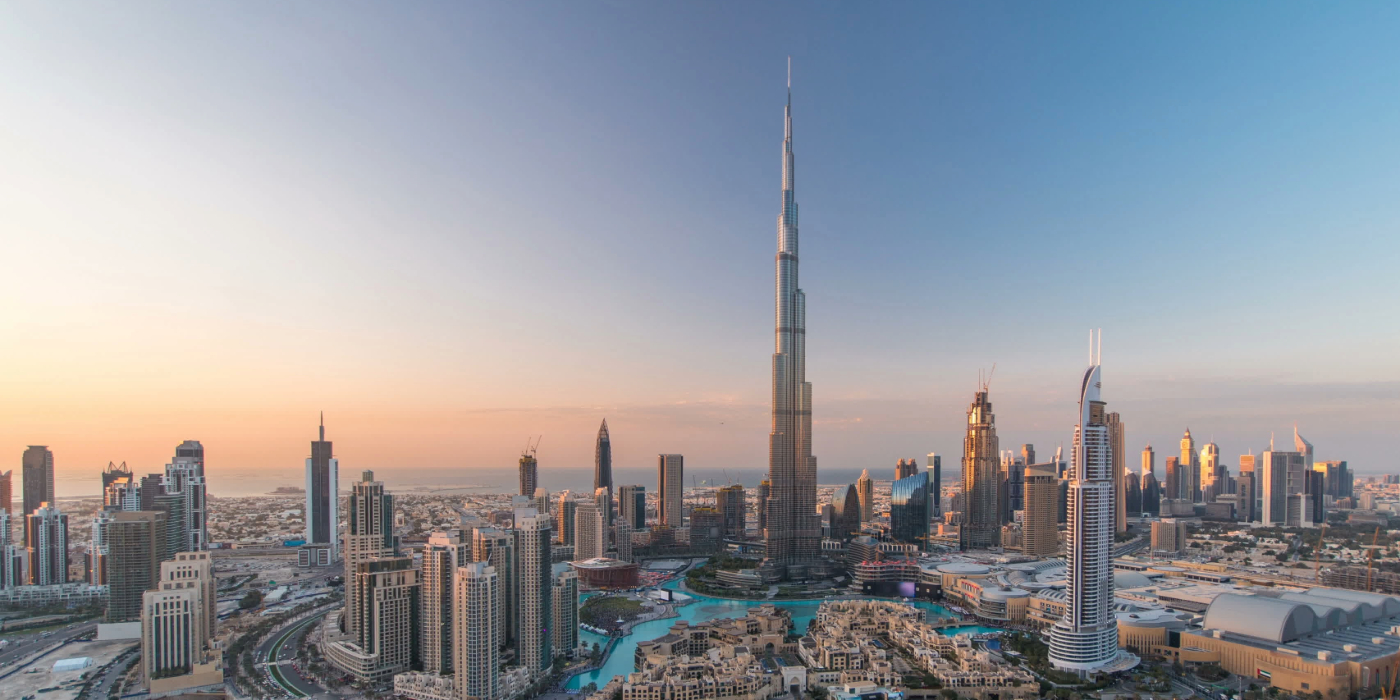 The Dubai skyline at sunset, featuring towering buildings illuminated by warm hues of orange and pink.