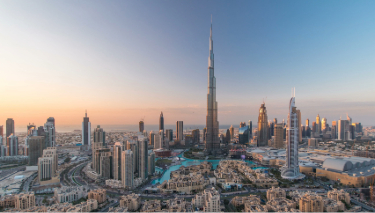 The Dubai skyline at sunset, featuring towering buildings illuminated by warm hues of orange and pink.