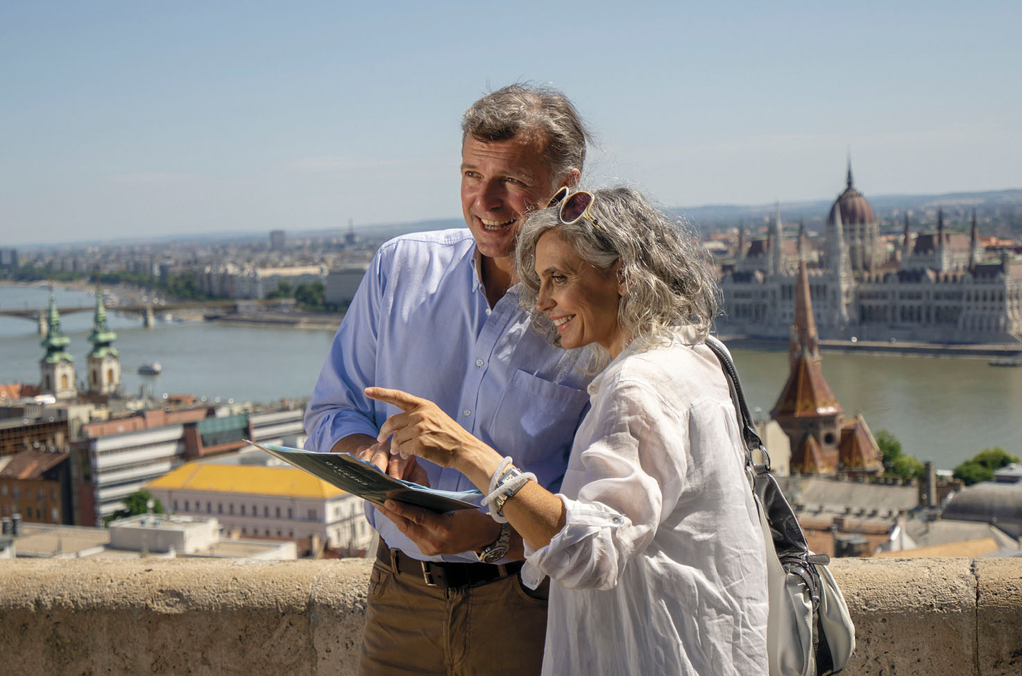 Couple looking at a guidebook and smiling while in Budapest, with the Danube River in the background