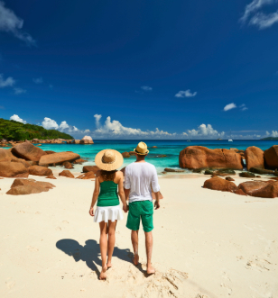 A couple pictured strolling along a white sand beach with blue skies