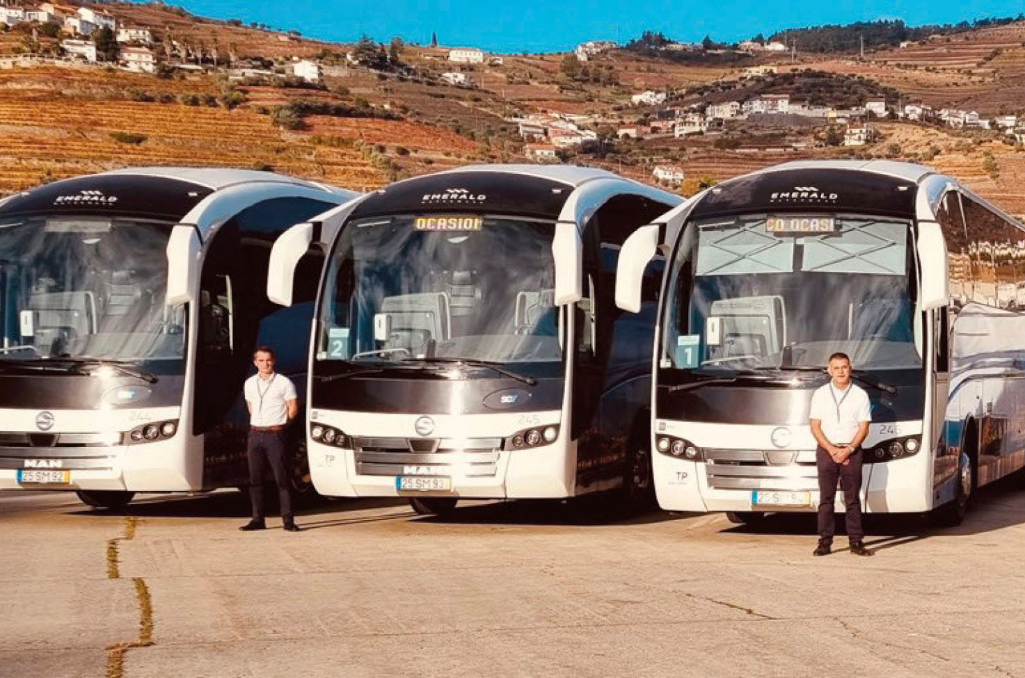 Four coach drivers standing next to three coaches, with the Portuguese hills in the background