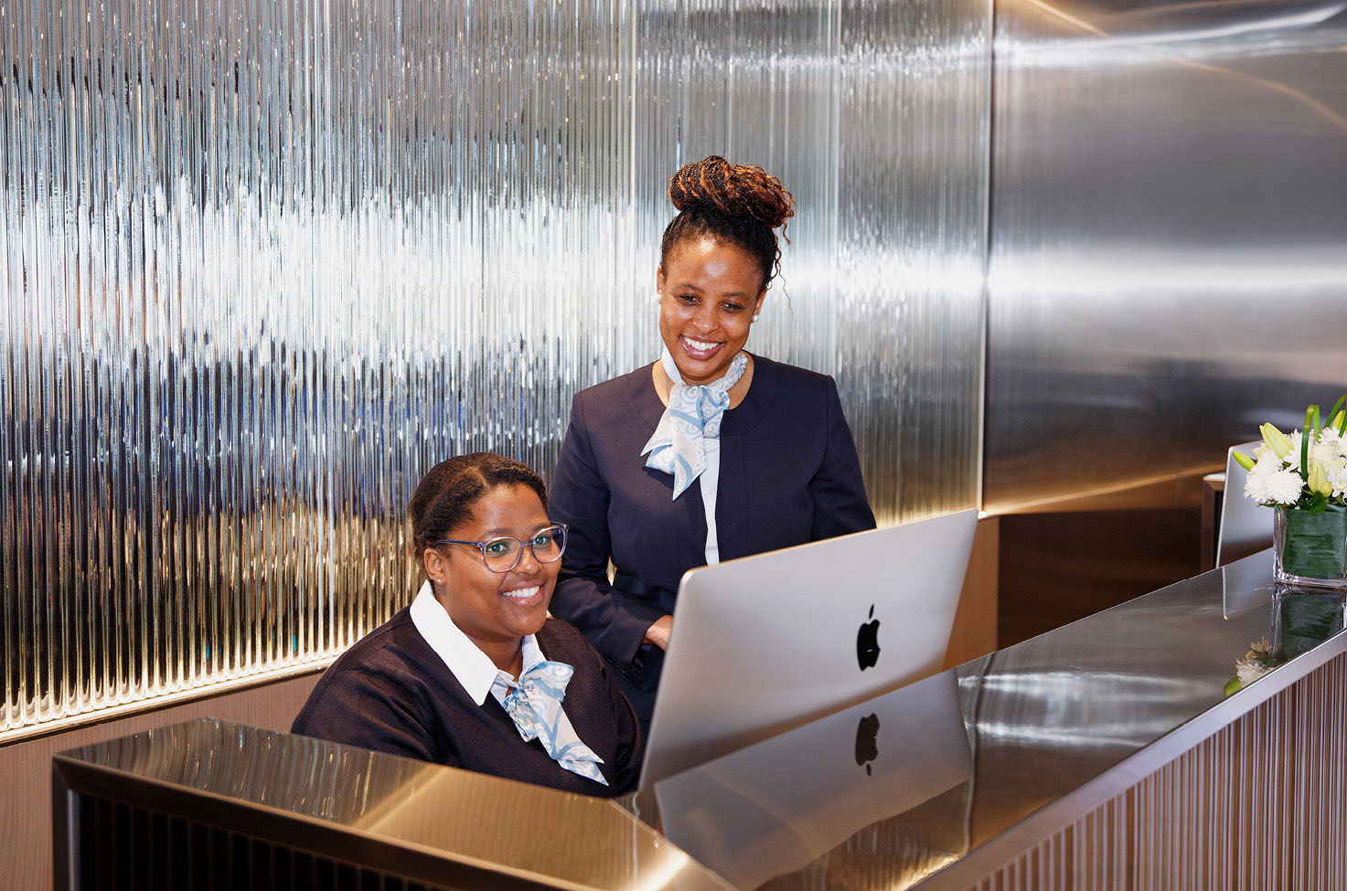 Two smiling receptionists, behind their well-polished desk, looking at a computer monitor