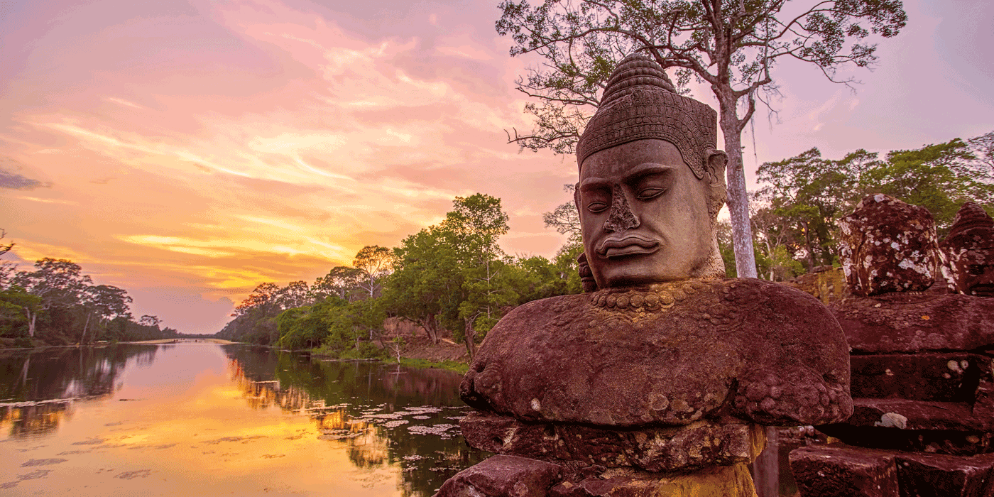 statue of a face next to the mekong river next to some trees under a yellow and purple sunset
