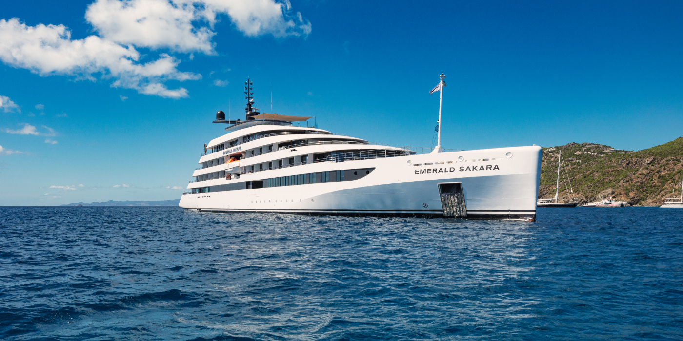 A large white boat named Emerald Sakara is floating in the water under a partly cloudy sky.