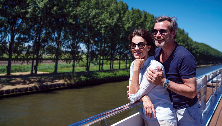 Couple stood on the Sun Deck of a luxury river ship, admiring the passing landscapes