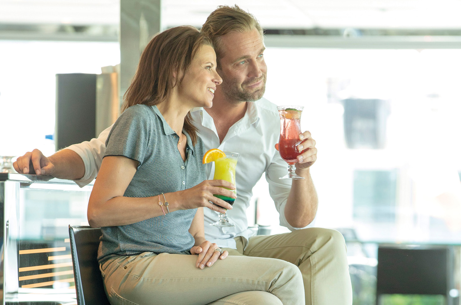 Couple in smart, casual dress sat at the bar enjoying a cocktail on board an Emerald Cruises river ship sailing through Europe