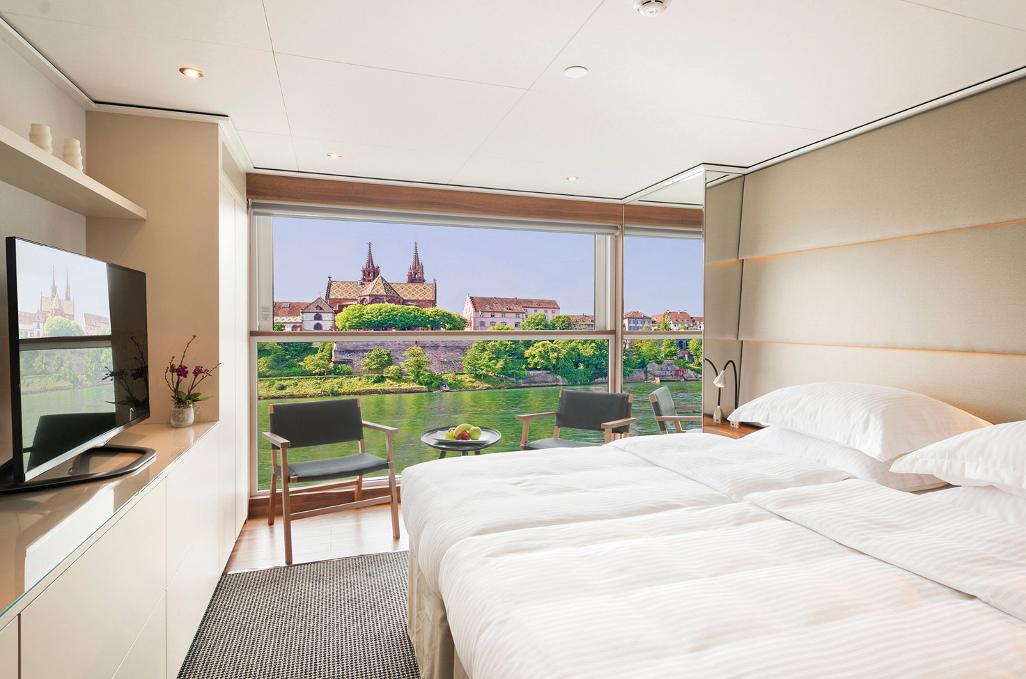A modern balcony suite with a crispy white queen size bed, tv, and comfortable seating on board an Emerald Cruises river ship sailing through the heart of Europe. 