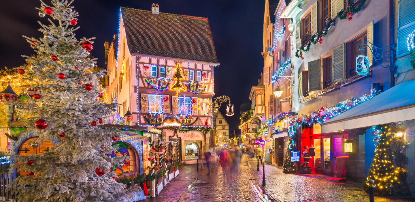 The old town of Colmar. Alsace in France decorated in sparkling Christmas lights and Christmas trees either side of  a cobbled street.