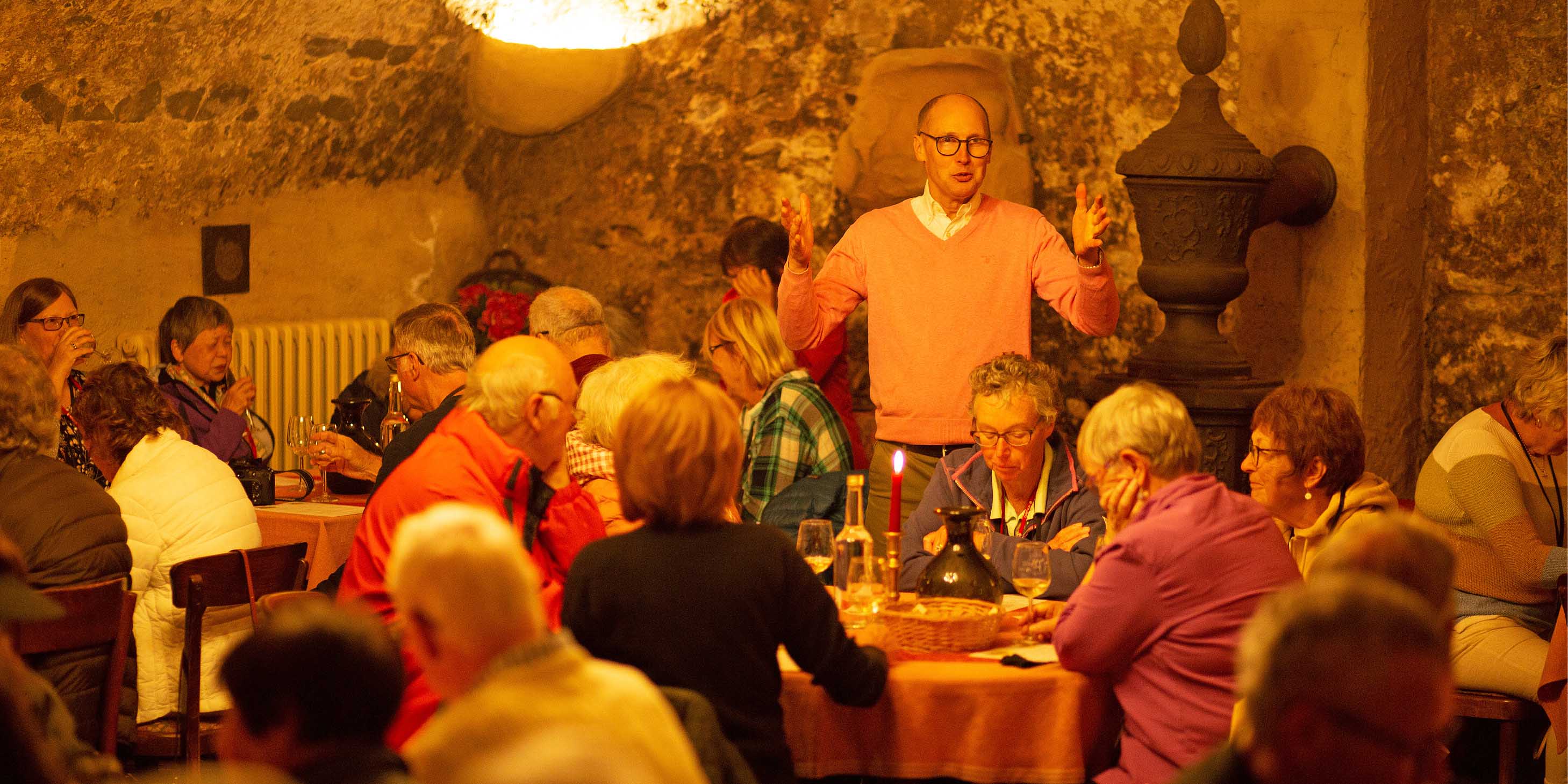 Wine connoisseur hosting a wine tour and tasting session in Bernkastel wine cellar, with many guests seated in the ambiently lit space