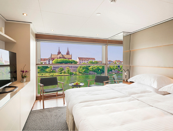 A panoramic view can be seen in this cruise ship accommodation. The bed has fresh white linen, with chairs available to take in the breathtaking view