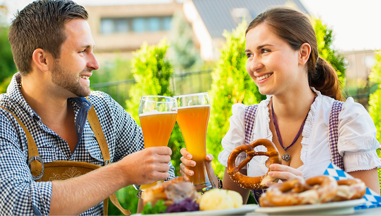 Man and woman drinking a pint of beer and eating a pretzel in traditional Bavarian clothes