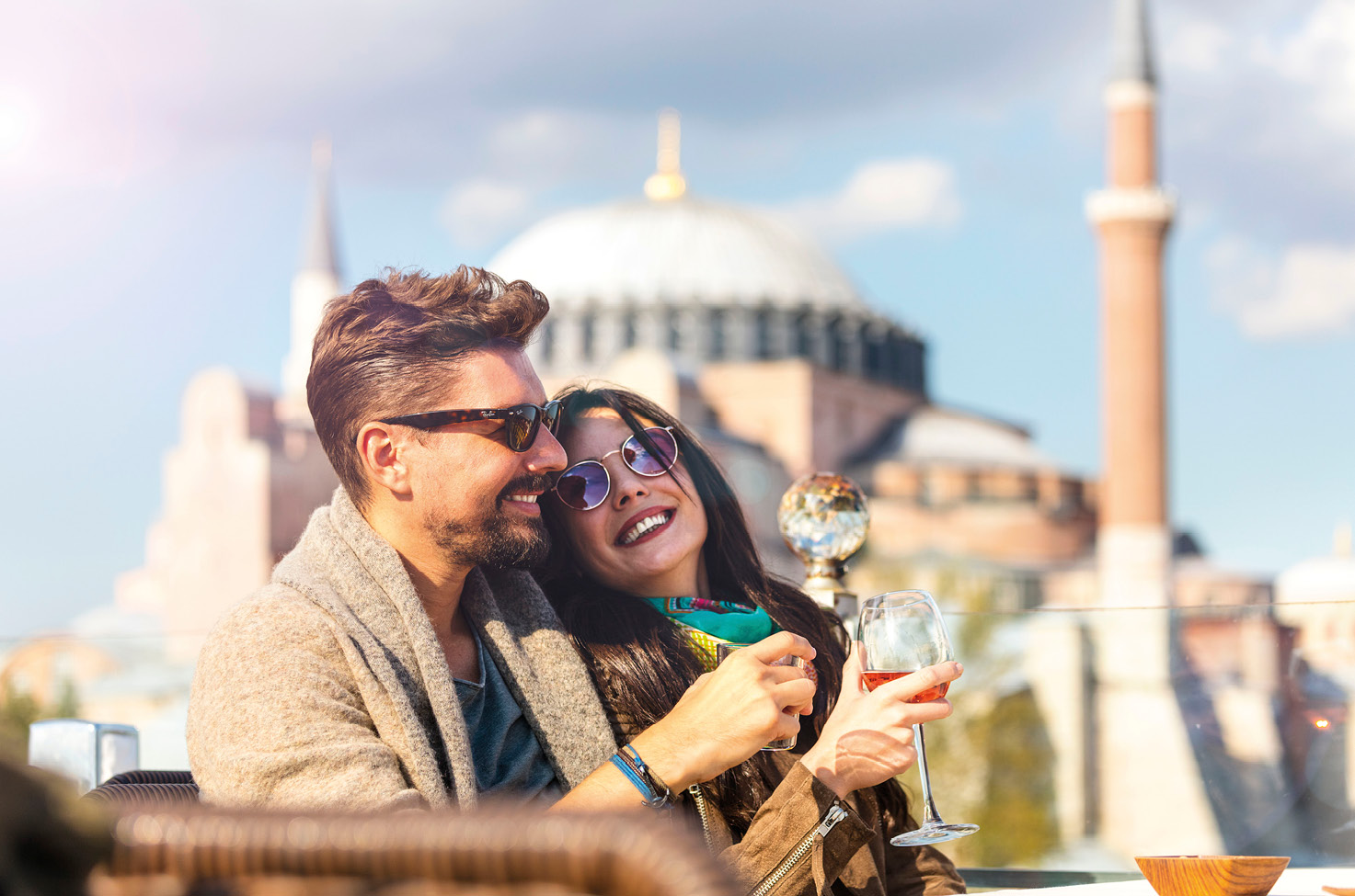 A smiling couple each enjoy a glass of wine on a balcony with views of Istanbul’s Sultanahmet in the background