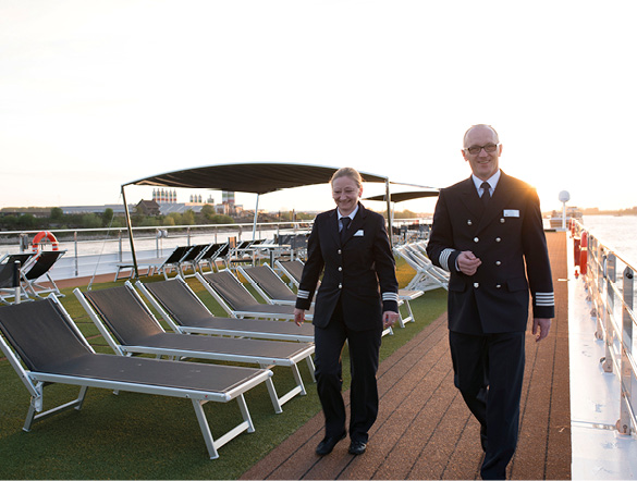 Two senior cruise ship staff walking the top deck past a row of sun loungers as the sun begins to set