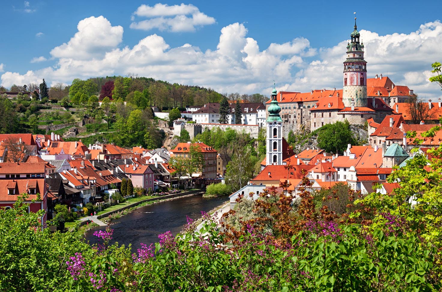 Cesky Krumlov, with white, orange-roofed buildings, trees, and blue cloudy sky