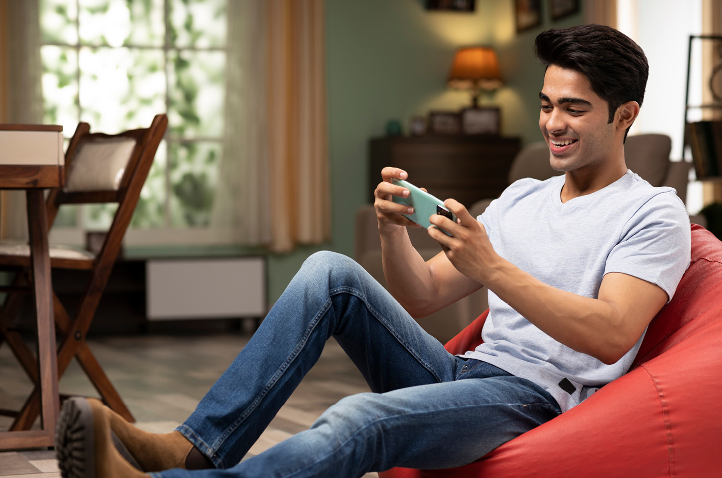 Man in white shirt sat on a beanbag and smiling as he looks at his phone