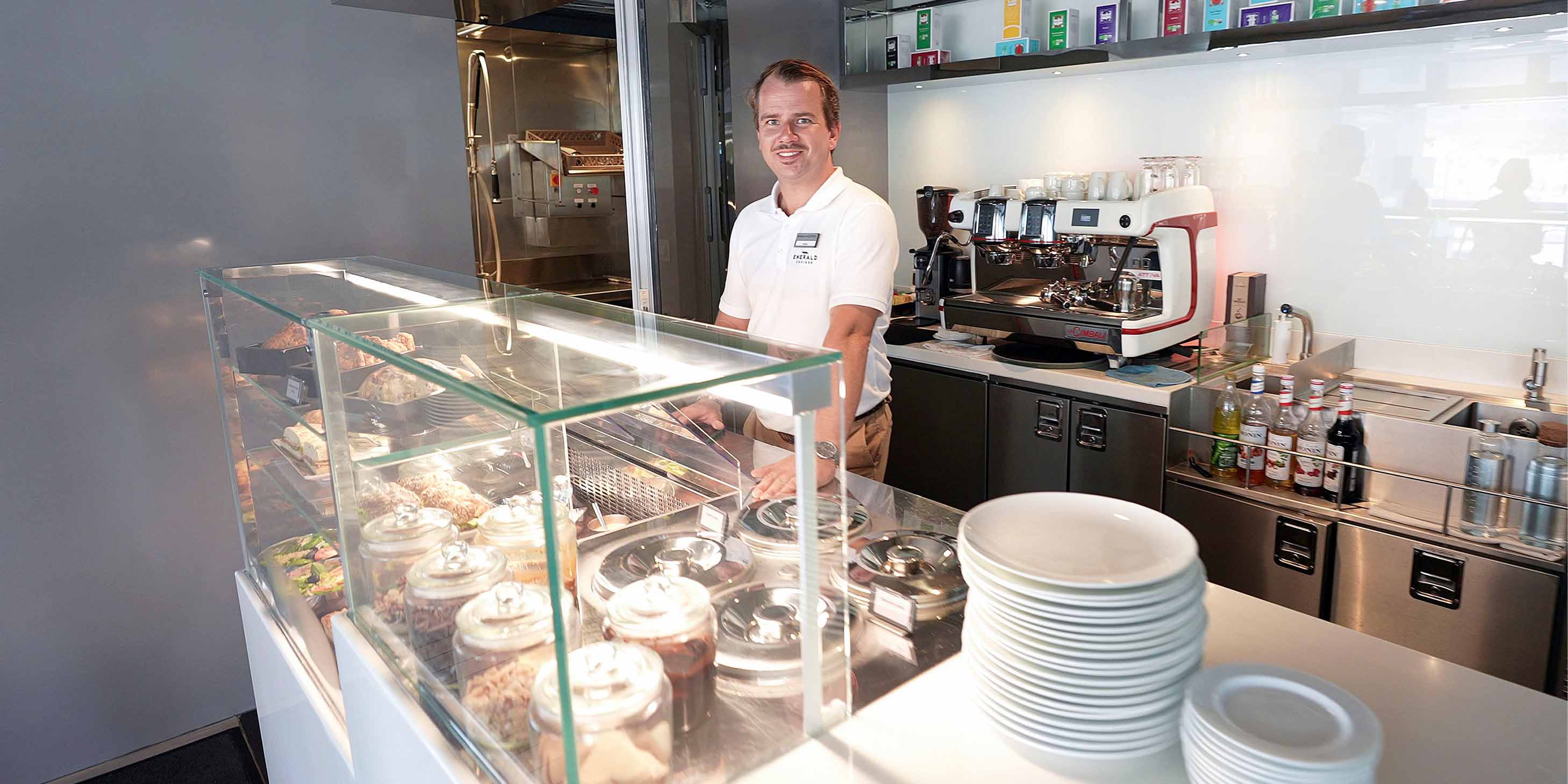 A server standing behind the counter and smiling, with a range of dishes and clean plates next to him