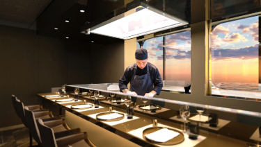 A Japanese chef preparing food at an empty private dining table under a bright light