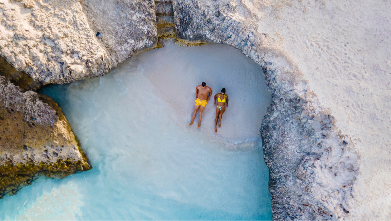 Couple relaxing on a secluded white sandy beach in the Caribbean overlooking crystal-clear azure waters