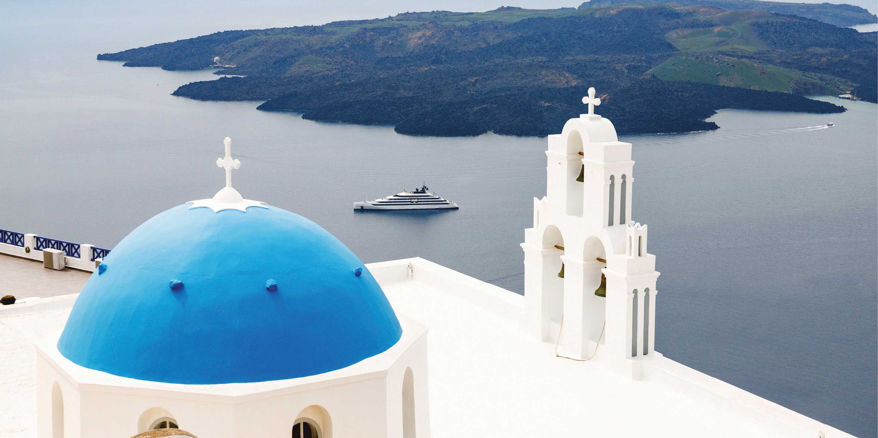 Luxury yacht sailing near the coast of Santorini surrounded by the iconic whitewashed buildings with blue rooftops