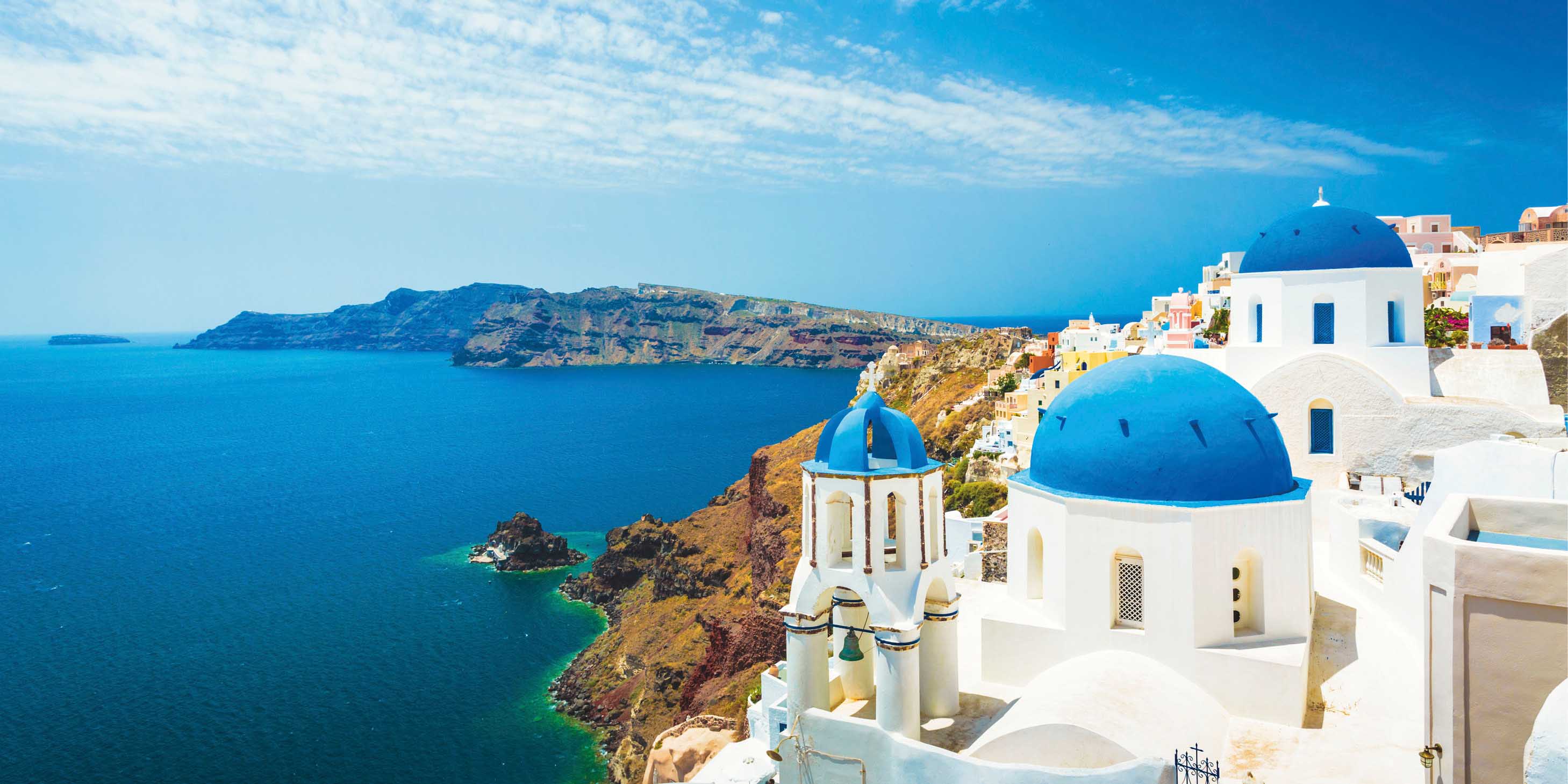 Blue-domed church of Santorini, Greece on a bright sunny day, with light cloudy sky and deep blue sea