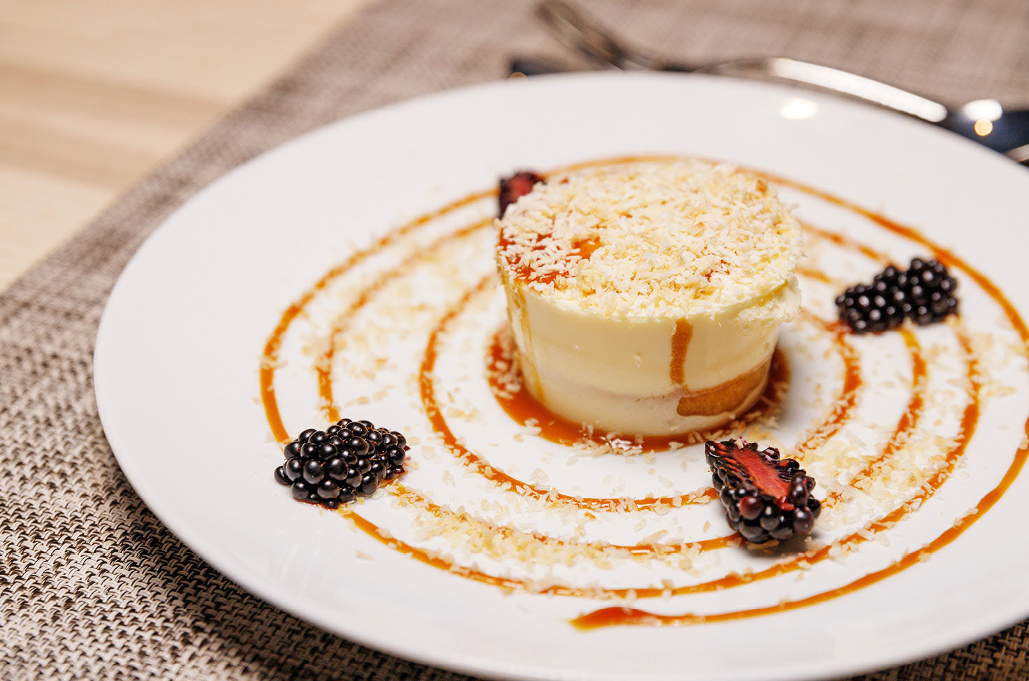 A delicious summer dessert sits on a white plate, with blackberries and a fruit coulis used to decorate the dish