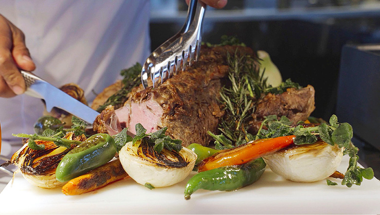 Chef cutting delicious meat surrounded by fresh local produce for guests on board an Emerald Cruises luxury yacht cruise