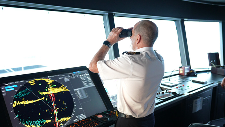 Captain looking out of binoculars towards the horizon from the navigation bridge of an Emerald Cruises luxury yacht cruise